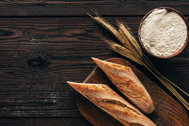 pohled shora naaranžované francouzská bageta na prkénku, pšenice a mouku v míse na dřevěný povrch - Fotografie, Obrázek