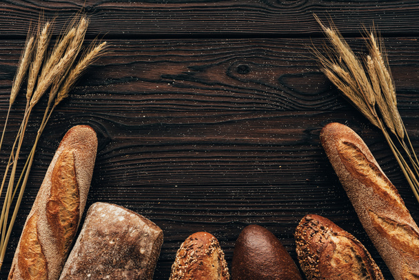 top view of arranged loafs of bread and wheat on wooden surface - Photo, Image