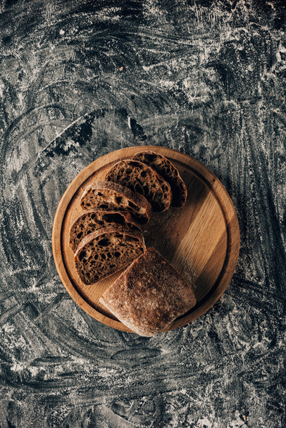 κάτοψη του τοποθετημένα κομμάτια του ψωμιού στην κοπή του σκάφους στην σκοτεινή επιφάνεια με αλεύρι - Φωτογραφία, εικόνα