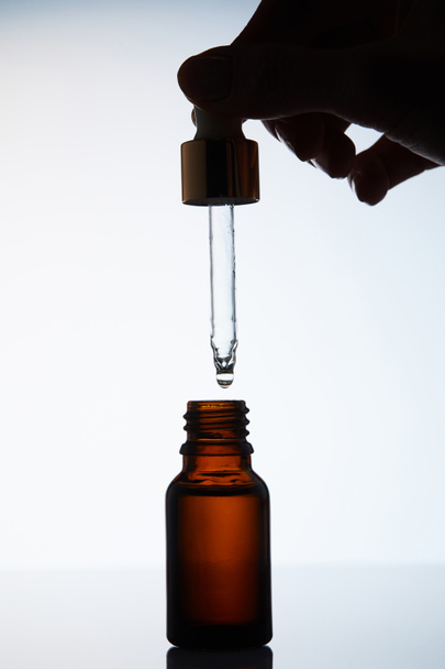 tiro recortado de la mujer dejando caer aceite aromático en botella de la pipeta en blanco
 - Foto, Imagen