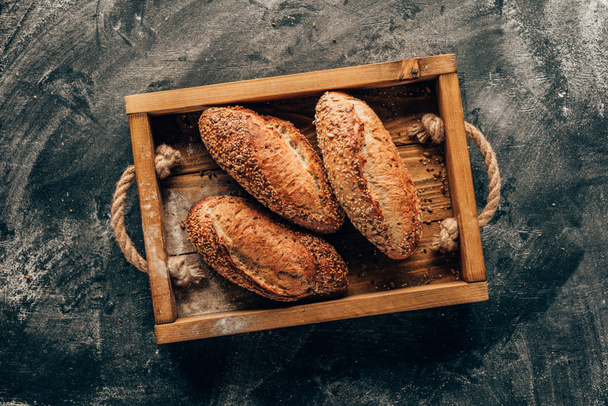 top view of arranged loafs of bread in wooden box on dark tabletop with flour - Fotoğraf, Görsel