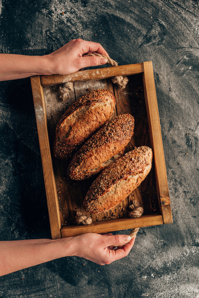 cropped shot of woman holding wooden box with loafs of bread in hands - Foto, afbeelding