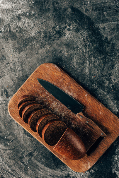 top view of arranged pieces of bread on cutting board with knife on dark surface with flour - Fotoğraf, Görsel