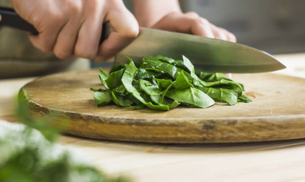 A woman is cutting spinach on a kitchen board. - Zdjęcie, obraz