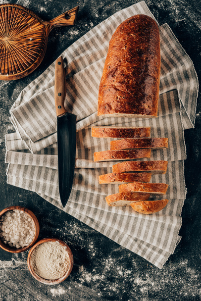 flache Lage mit Brotstücken auf Leinen und Schüsseln mit Mehl in der Nähe auf dunkler Tischplatte - Foto, Bild
