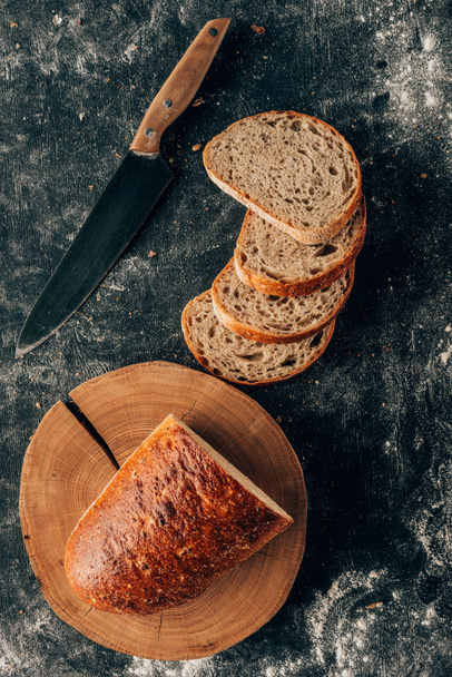 top view of arranged pieces of bread and knife on dark tabletop with flour - Foto, Imagen