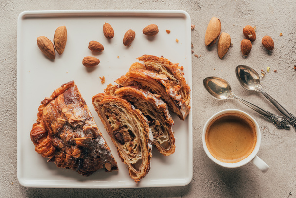 top view of cup of coffee and sweet pastry with almonds on plate on light tabletop - Foto, afbeelding