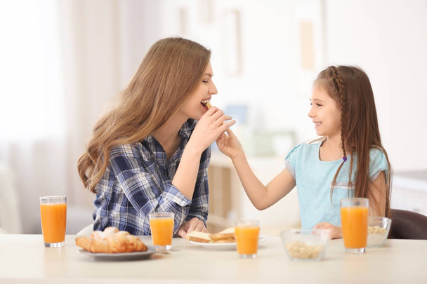 Mother with daughter having breakfast in kitchen - Фото, изображение