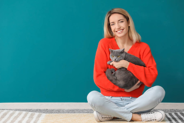 Young woman with cute pet cat against color wall - Foto, imagen