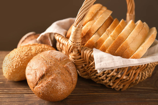 Wicker basket with sliced bread and fresh buns on wooden table - Фото, изображение