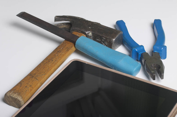 Tablet and working tools. On the white surface of the table is a tablet, skein, chisel and pliers. Destruction and repair of electronic devices. - Foto, immagini