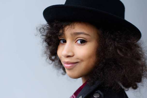 close-up portrait of happy child with curly hair in hat isolated on grey - Photo, Image