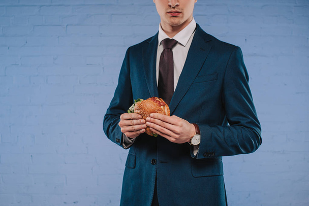 cropped shot of young businessman in suit holding burger - Photo, Image