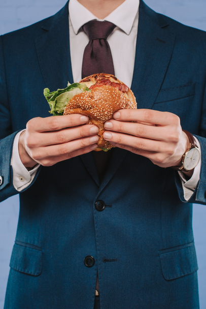 ハンバーガーを保持しているフォーマルなスーツのビジネスマンのクロップ撮影 - 写真・画像