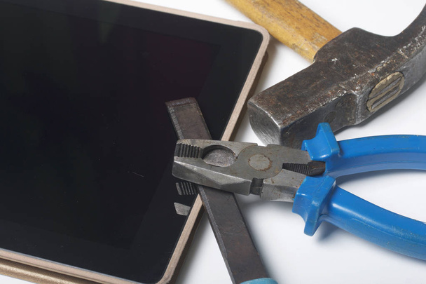 Tablet and working tools. On the white surface of the table is a tablet, skein, chisel and pliers. Destruction and repair of electronic devices. - Fotografie, Obrázek