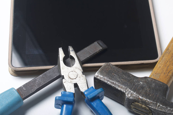 Tablet and working tools. On the white surface of the table is a tablet, skein, chisel and pliers. Destruction and repair of electronic devices. - Foto, immagini