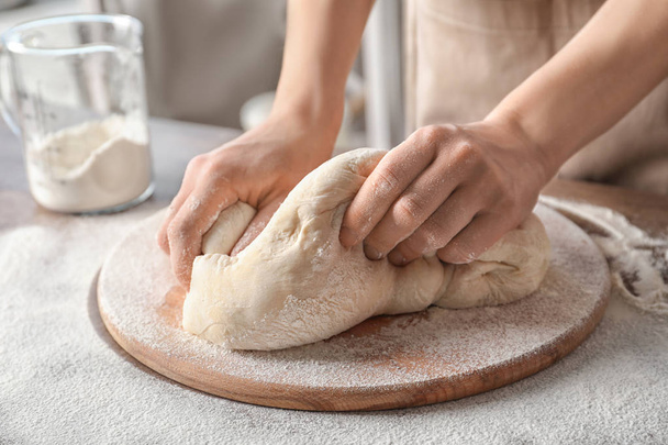 Woman kneading dough on wooden board sprinkled with flour - 写真・画像