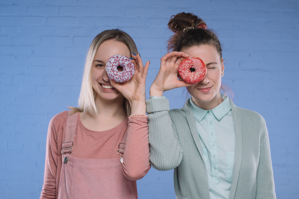 giovani donne sorridenti che coprono gli occhi con ciambelle smaltate
 - Foto, immagini
