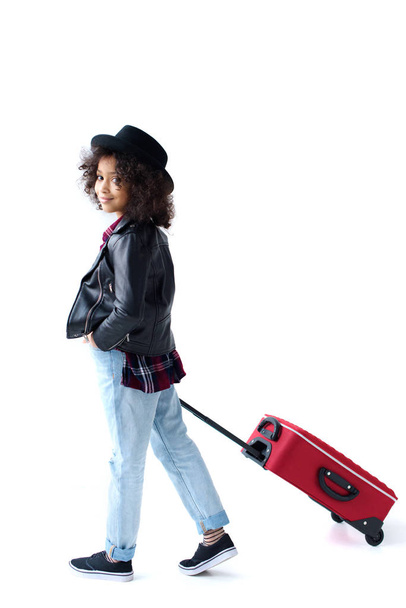 vista lateral de un niño pequeño y elegante caminando con equipaje aislado en blanco
 - Foto, Imagen