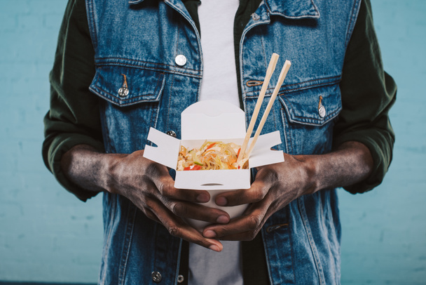 中華麺の箱を持ってのデニム ジャケットのアフリカ系アメリカ人のショットをトリミング - 写真・画像