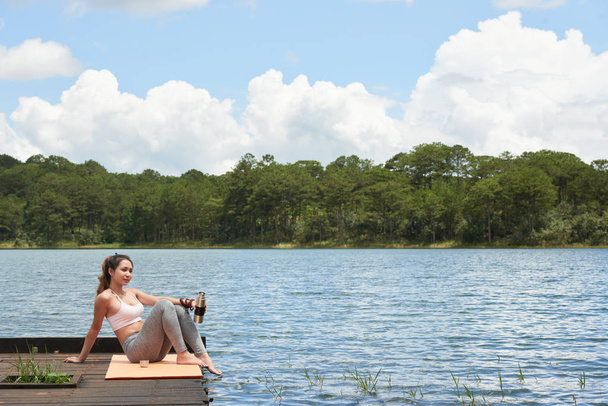 Belle jeune femme yogi boire du thé et assis au bord du lac
 - Photo, image