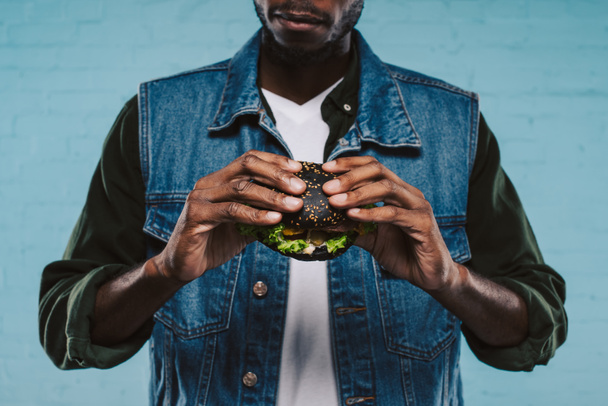 обрізаний знімок афроамериканця, що тримає смачний чорний бургер
 - Фото, зображення