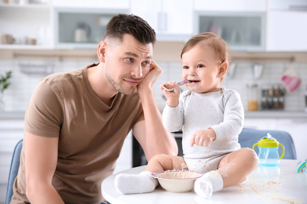 Father feeding his little son in kitchen - Foto, afbeelding