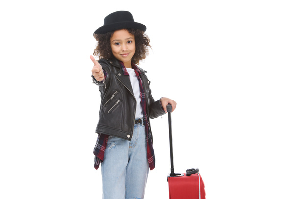 hermoso niño pequeño con equipaje mostrando el pulgar hacia arriba aislado en blanco
 - Foto, Imagen