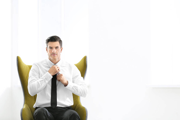 Handsome businessman sitting in comfortable armchair indoors - Фото, изображение
