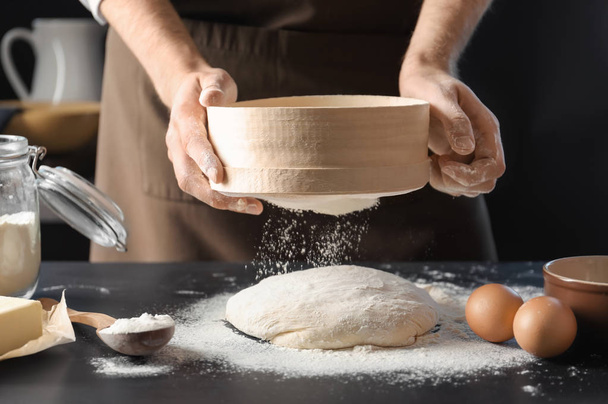 Man sifting flour over dough on table - Fotografie, Obrázek