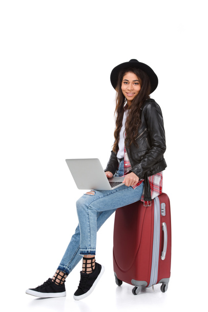 stijlvolle jongedame met behulp van laptop zittend op bagage geïsoleerd op wit - Foto, afbeelding