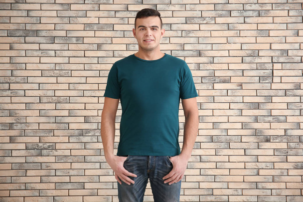 Young man in stylish t-shirt on brick wall background. Mockup for design - Foto, Imagen