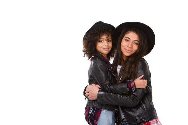 beautiful embracing mother and daughter in leather jackets and hats mother and daughter isolated on white - Foto, Bild