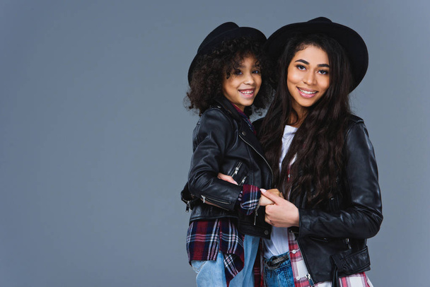 young embracing mother and daughter in leather jackets isolated on grey - Photo, image