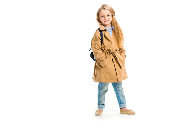 Child in glasses wearing beige trench coat and holding bag isolated on white - 写真・画像