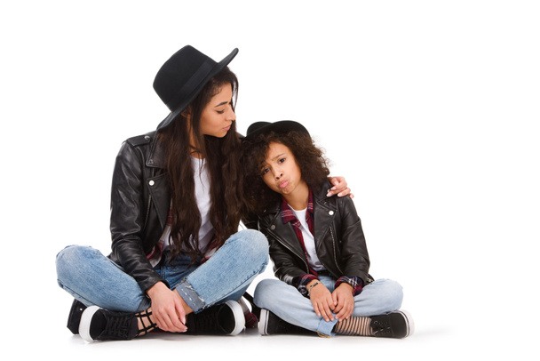 belle mère et fille en vestes en cuir et chapeaux assis sur le sol isolé sur blanc
 - Photo, image
