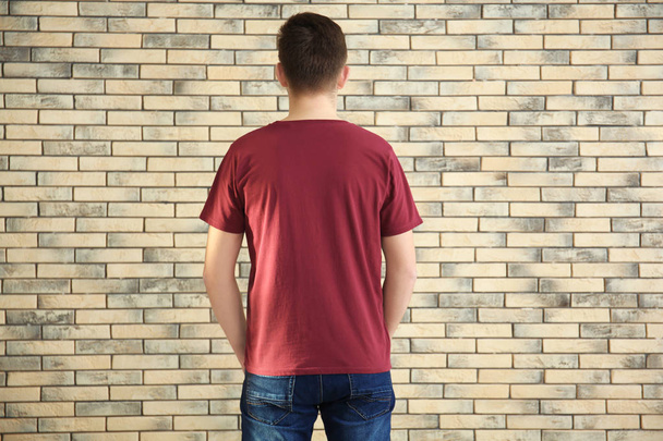 Young man in stylish t-shirt on brick wall background. Mockup for design - 写真・画像