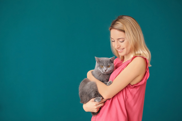 Young woman with cute pet cat on color background - 写真・画像