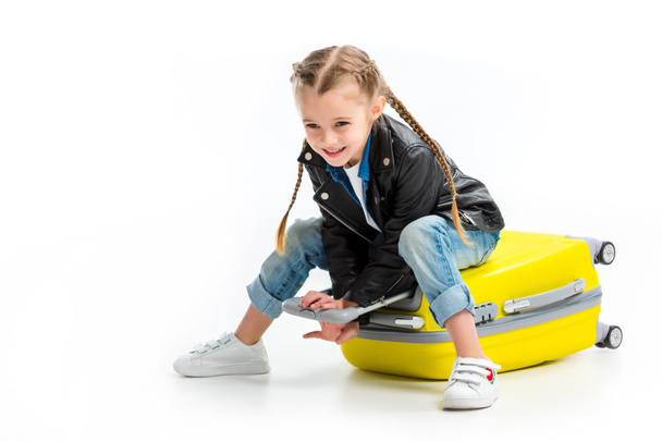 Child with pigtails sitting on lying wheel suitcase isolated on white - Fotó, kép
