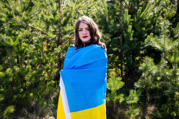 El modelo en ropa negra sostiene la bandera de Ucrania. Envuelto en una bandera
 - Foto, imagen