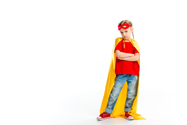 Pequeña superchica gruñona usando capa amarilla con máscara roja para los ojos en la frente aislada en blanco
 - Foto, Imagen