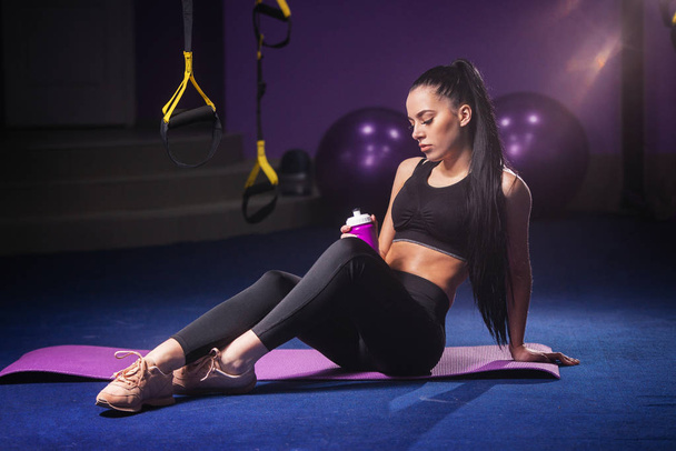 Kobieta Sport siedzieć i odpoczywać po treningu lub poćwiczyć w siłowni fitness z shake białka lub picie wody na podłodze. Zrelaksować się koncepcja. Trening siłowy i ciała budować tematu. - Zdjęcie, obraz