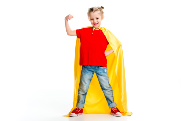 Smiling supergirl in yellow cape showing muscles on hand isolated on white - Foto, imagen