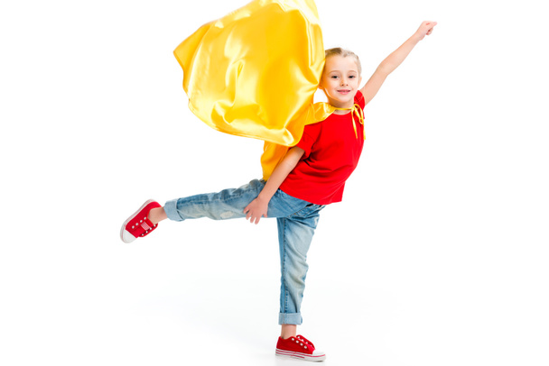 Pieni hymyilevä supertyttö keltainen viitta seisoo yhdellä jalalla ja eletään käsin eristetty valkoinen
 - Valokuva, kuva