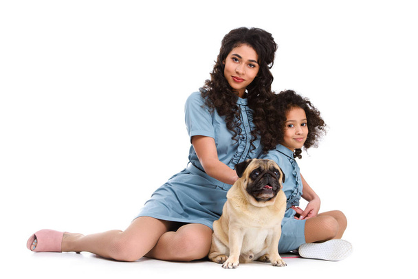 beautiful young mother and daughter sitting on floor with pug isolated on white - Foto, Bild