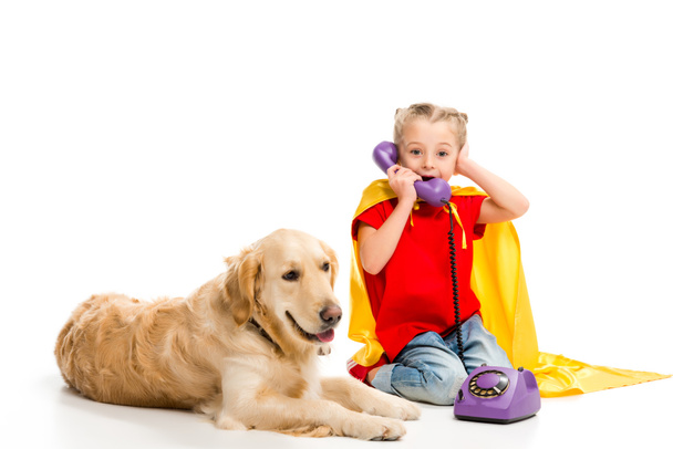 Lying golden retriever  with shocked little supergirl talking on phone isolated on white - Foto, immagini