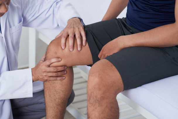 Nahaufnahme eines Arztes, der das Knie eines männlichen Patienten backt - Foto, Bild
