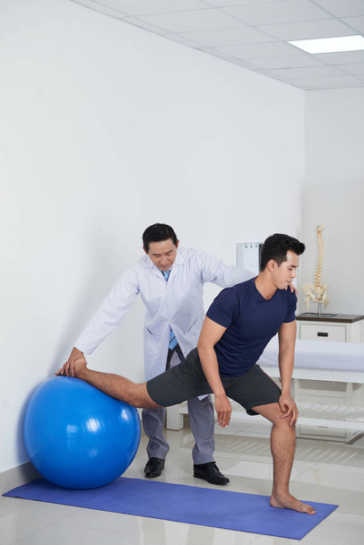 Physiothérapeute aidant le patient à faire de l'exercice sur le ballon de fitness
 - Photo, image