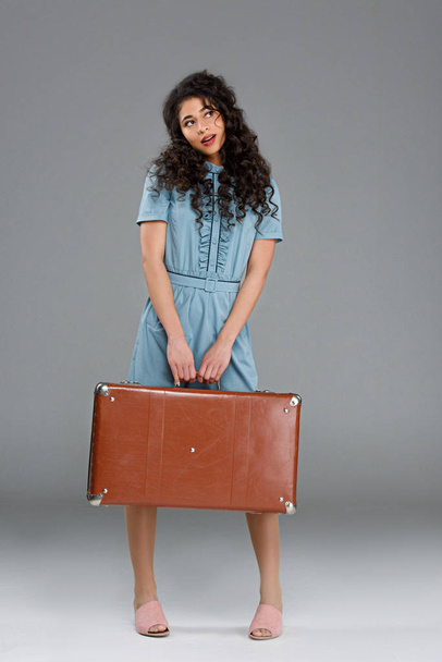 Nachdenkliche junge Frau mit Vintage-Koffer auf grau - Foto, Bild