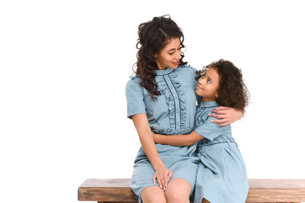 mother and daughter embracing while sitting on bench isolated on white - Photo, Image